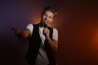 Photo of Talented young man singing on dark background with color light