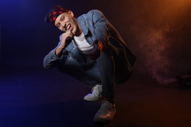 Photo of Talented singer performing on dark background with color lights and smoke