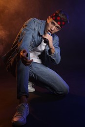 Photo of Talented singer performing on dark background with color lights and smoke