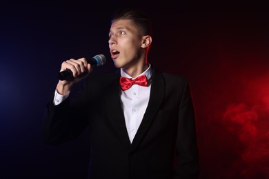 Photo of Talented singer performing on dark background with color lights and smoke