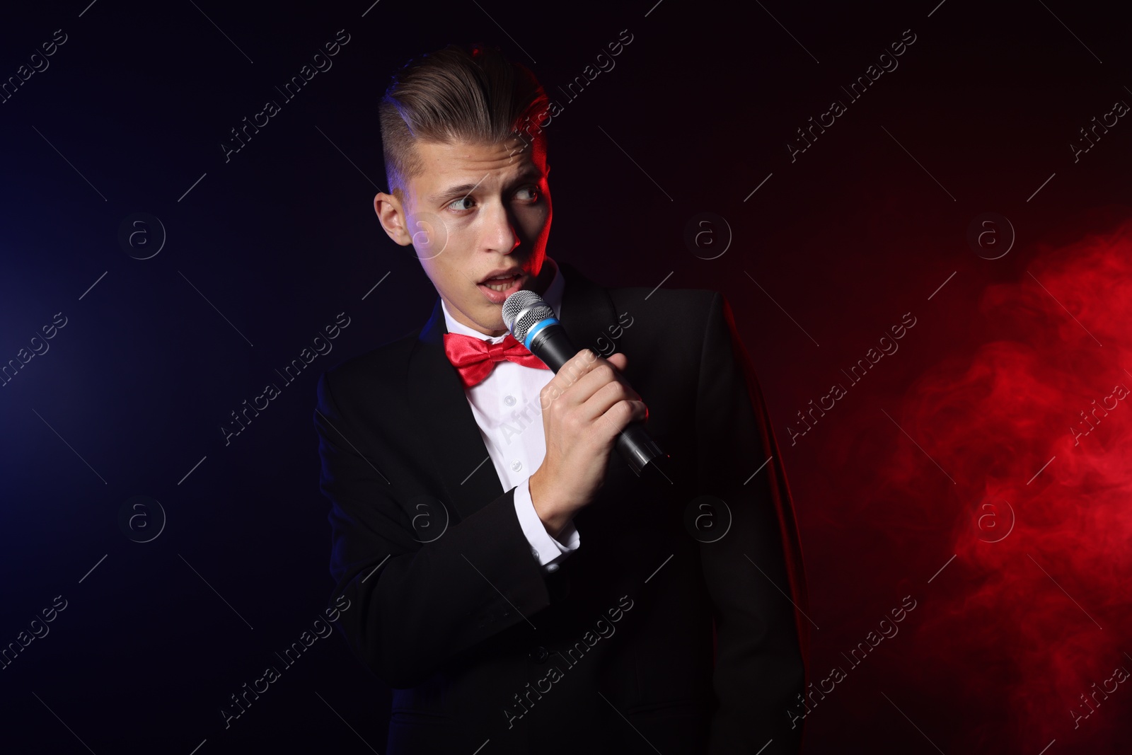 Photo of Talented singer performing on dark background with color lights and smoke