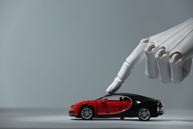 Photo of Artificial intelligence. Robot hand with toy car against grey background, closeup. Space for text