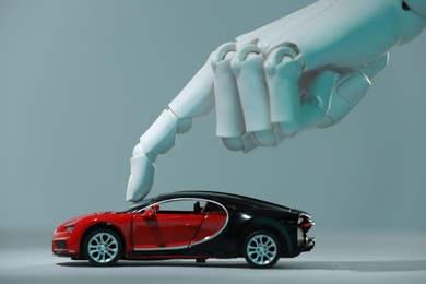 Photo of Artificial intelligence. Robot hand with toy car against grey background, closeup