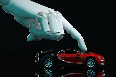 Photo of Artificial intelligence. Robot hand with toy car against black background, closeup