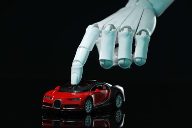 Photo of Artificial intelligence. Robot hand with toy car against black background, closeup