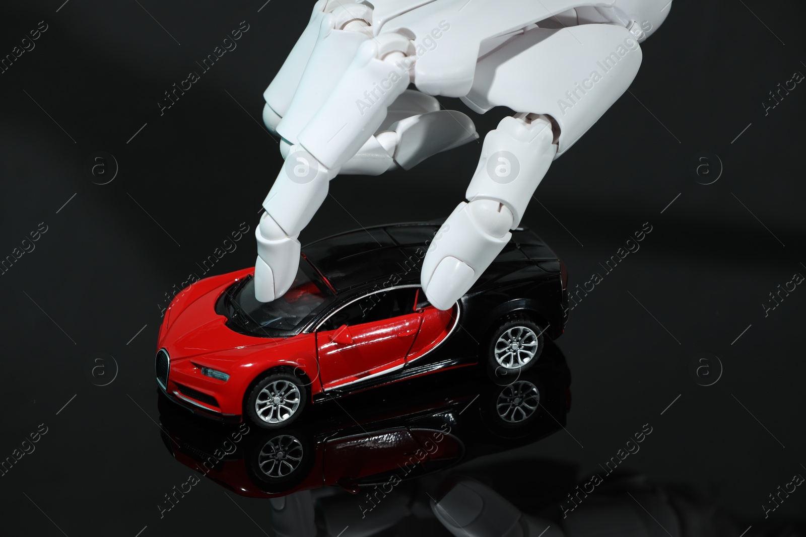 Photo of Artificial intelligence. Robot hand with toy car at black glass surface, closeup