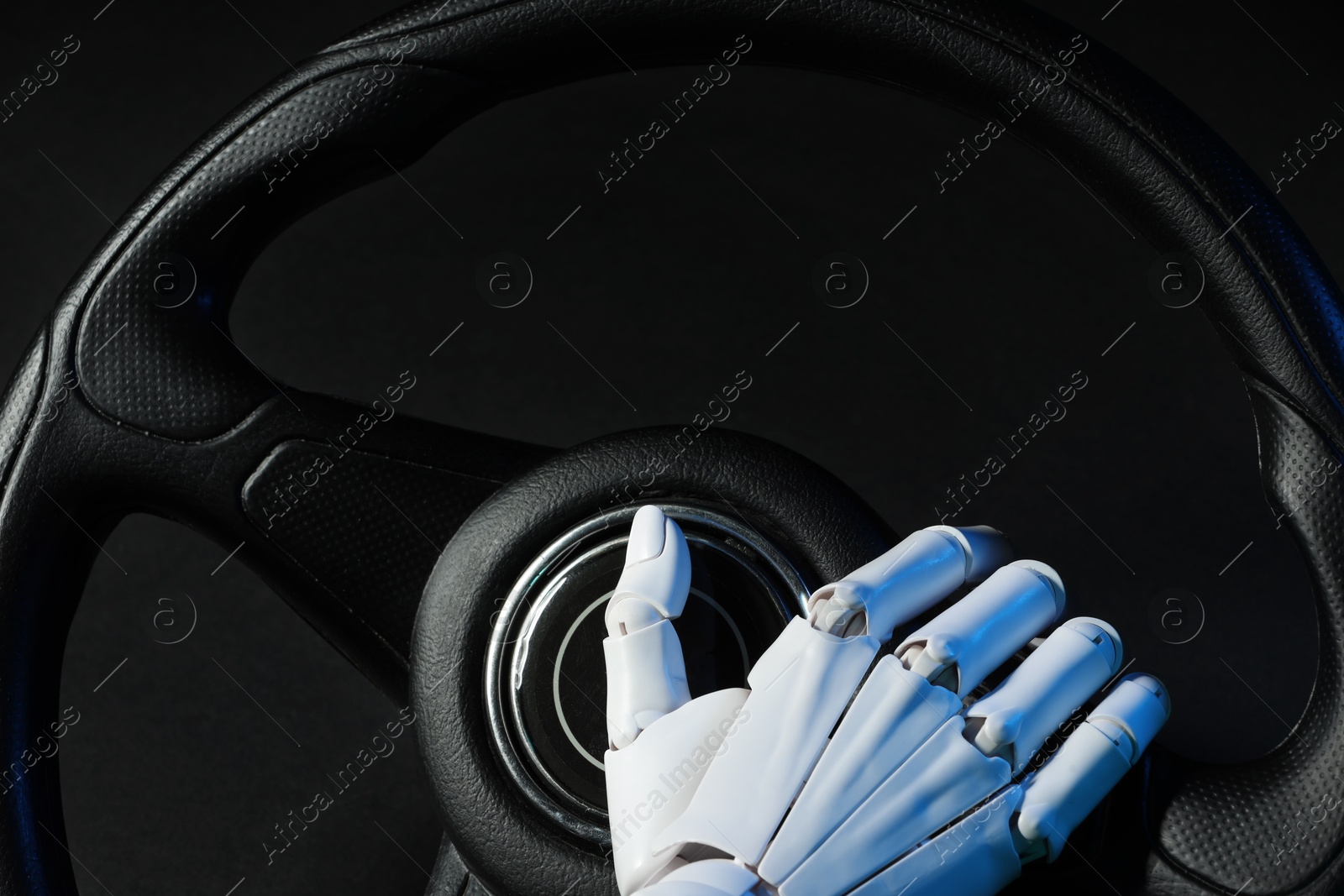 Photo of Artificial intelligence. Robot hand with steering wheel on black background in blue lights, closeup