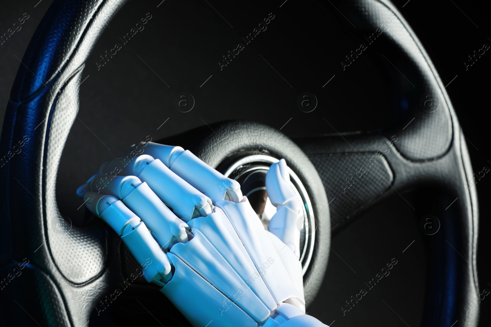 Photo of Artificial intelligence. Robot hand with steering wheel on black background in blue lights, closeup