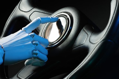 Photo of Artificial intelligence. Robot hand with steering wheel on black background in blue lights, closeup