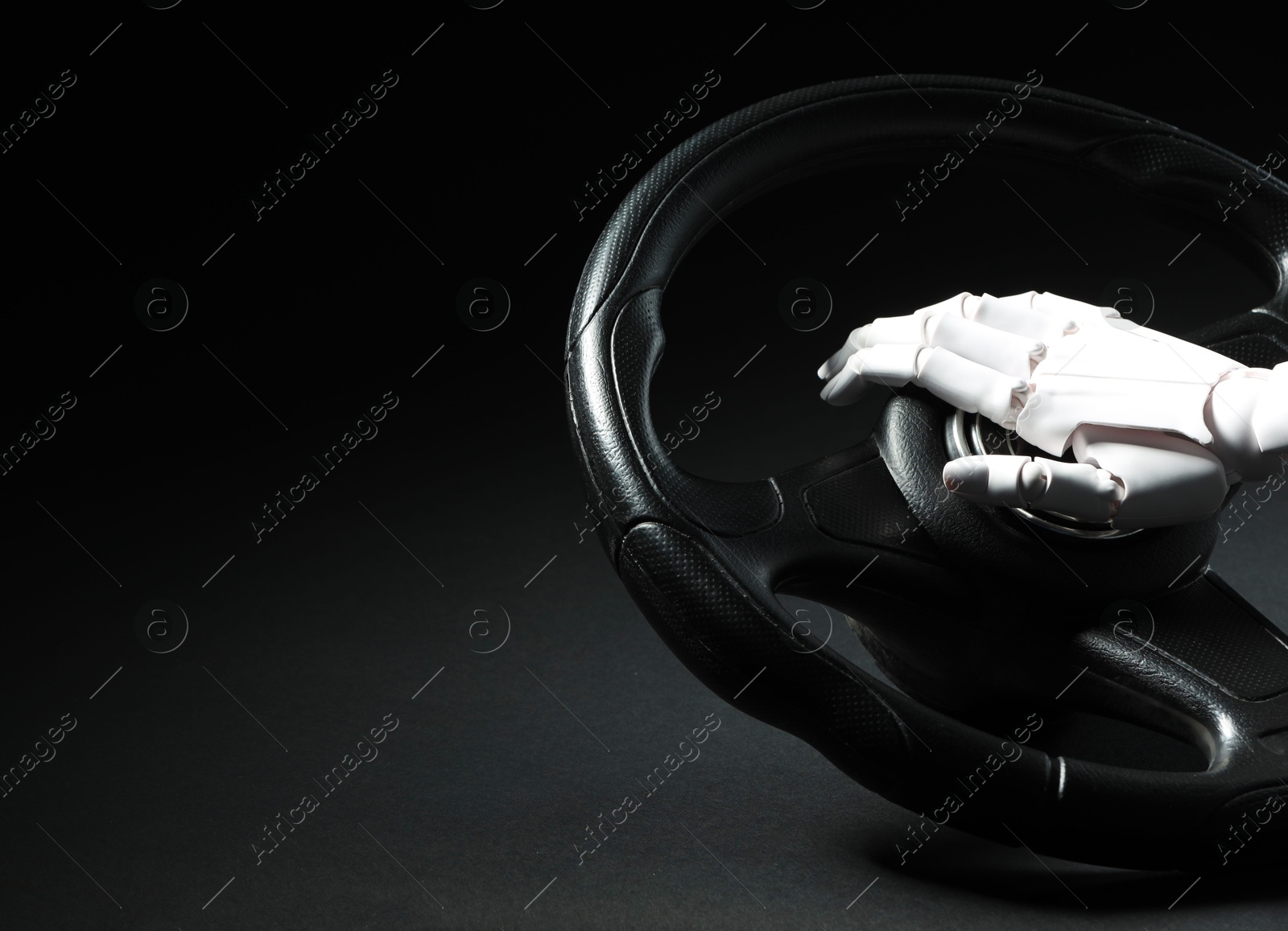 Photo of Artificial intelligence. Robot hand with steering wheel on black background, closeup. Space for text