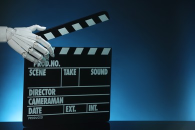 Photo of Artificial intelligence. Robot hand with clapper against dark blue background, closeup. Space for text