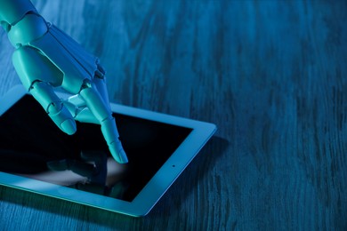 Photo of Artificial intelligence. Robot hand using tablet at wooden table, closeup