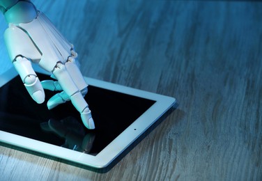 Photo of Artificial intelligence. Robot hand using tablet at wooden table, closeup. Space for text