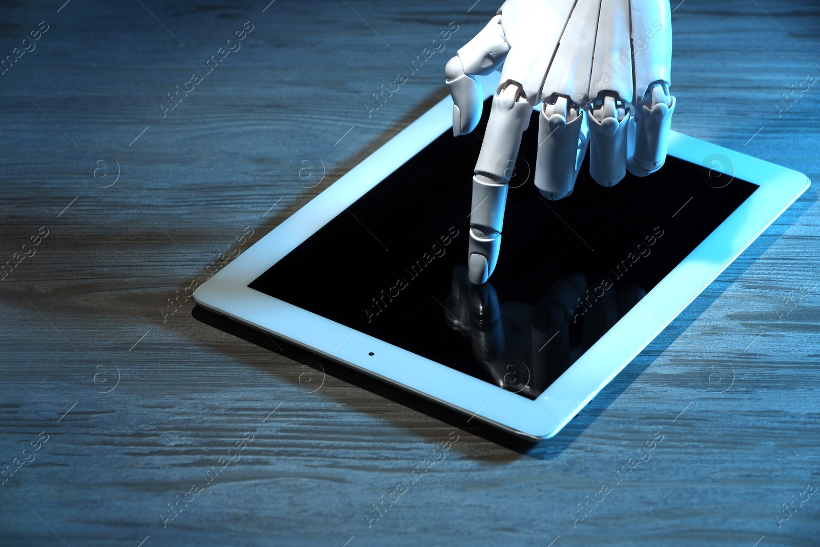 Photo of Artificial intelligence. Robot hand using tablet at wooden table, closeup