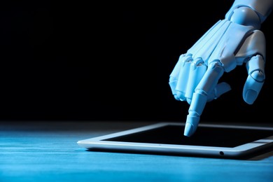 Photo of Artificial intelligence. Robot hand using tablet at wooden table, closeup. Space for text