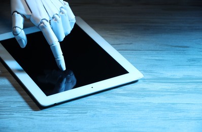 Photo of Artificial intelligence. Robot hand using tablet at wooden table, closeup. Space for text