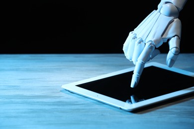 Photo of Artificial intelligence. Robot hand using tablet at wooden table, closeup. Space for text