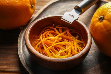 Photo of Orange zest, zester tool and fresh fruits on wooden table, closeup