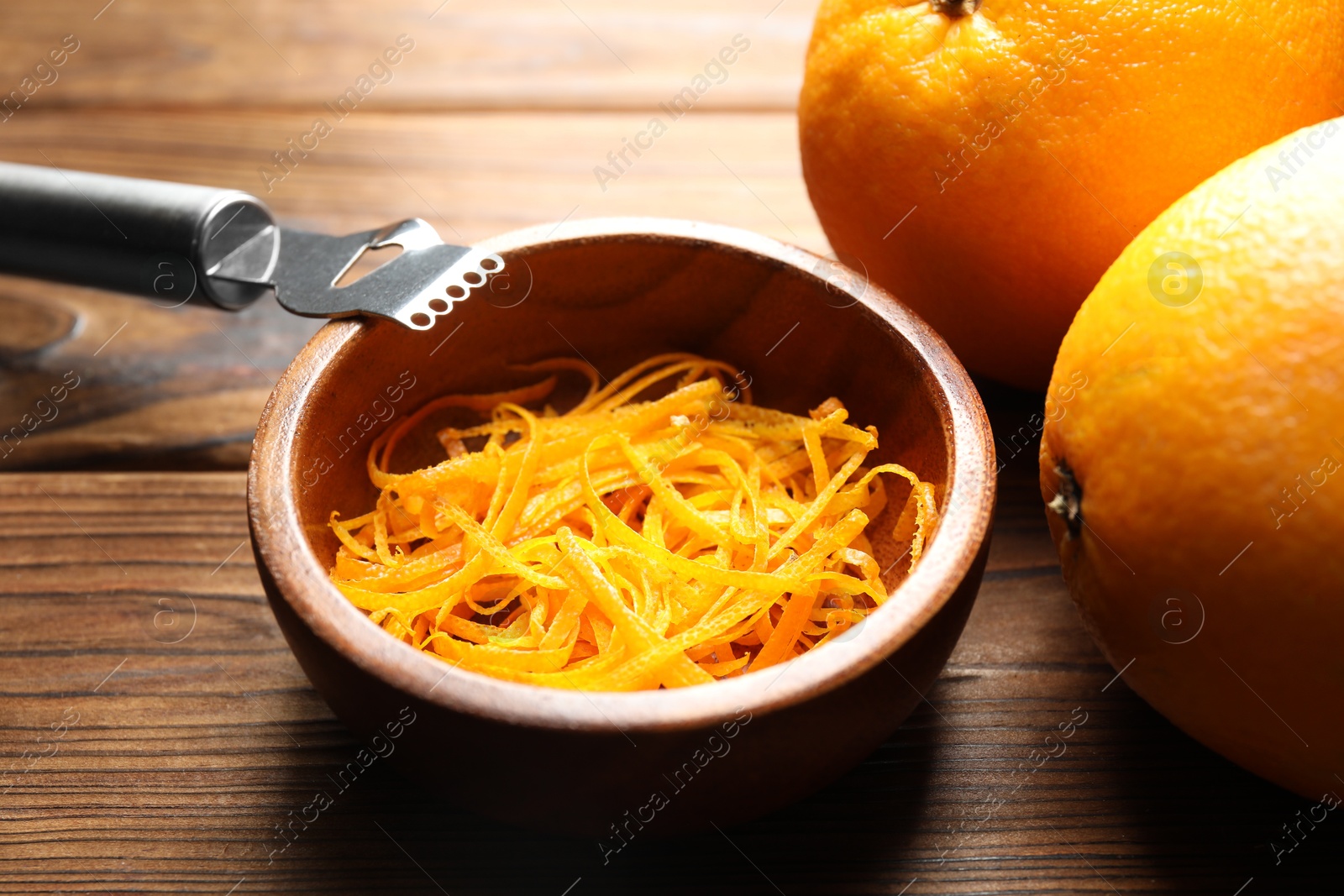 Photo of Orange zest, zester tool and fresh fruits on wooden table, closeup