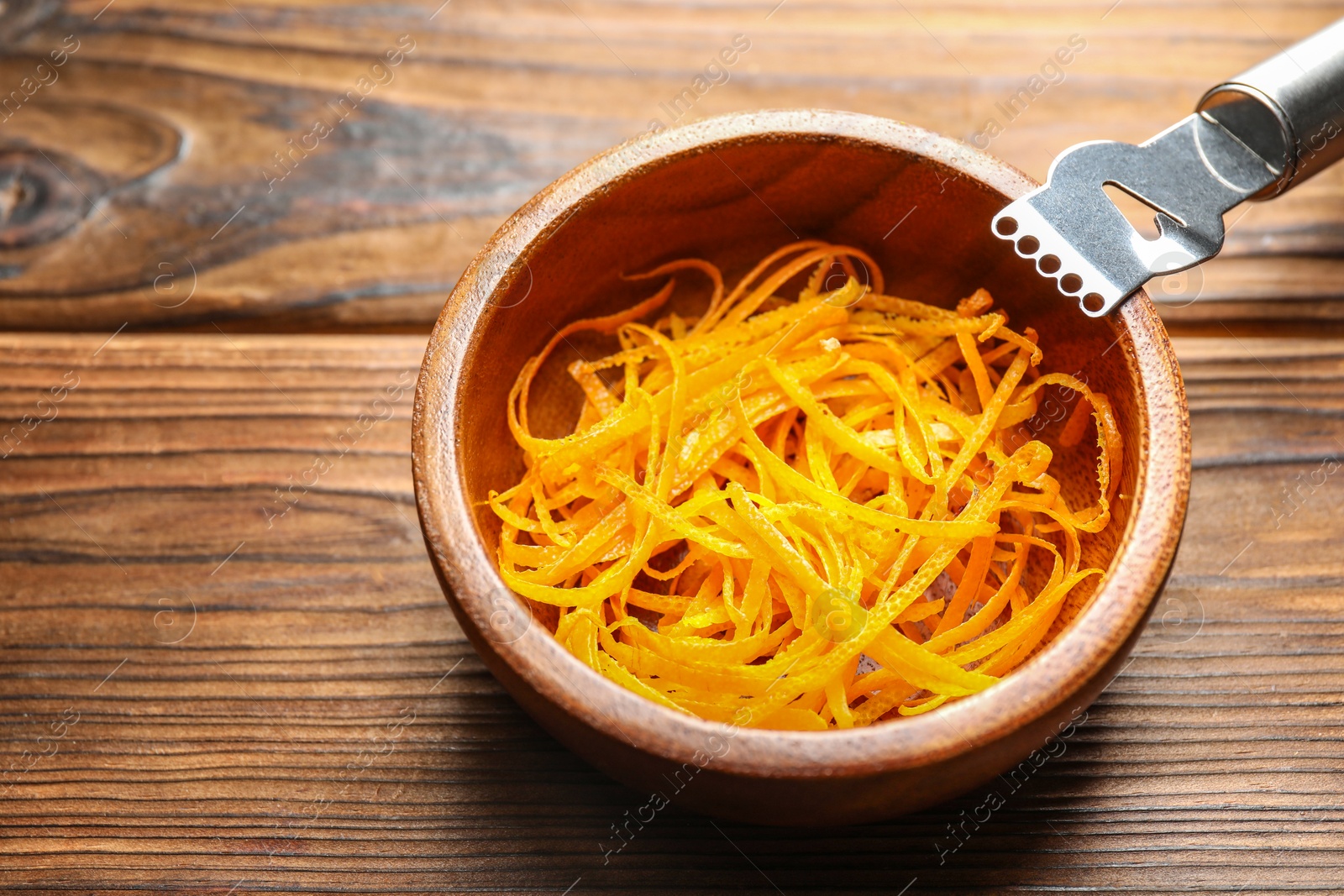 Photo of Fresh orange zest in bowl and zester tool on wooden table, closeup