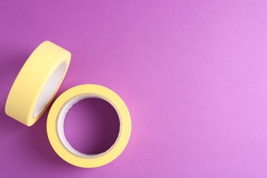 Photo of Rolls of masking tapes on violet background, top view. Space for text