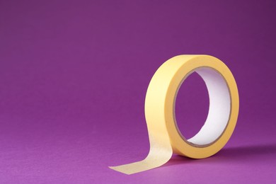 Roll of masking tape on violet background, space for text