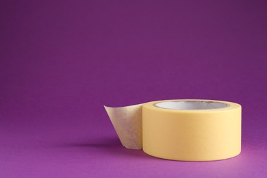 Photo of Roll of masking tape on violet background, space for text