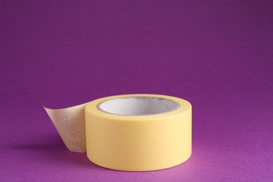 Photo of Roll of masking tape on violet background, space for text