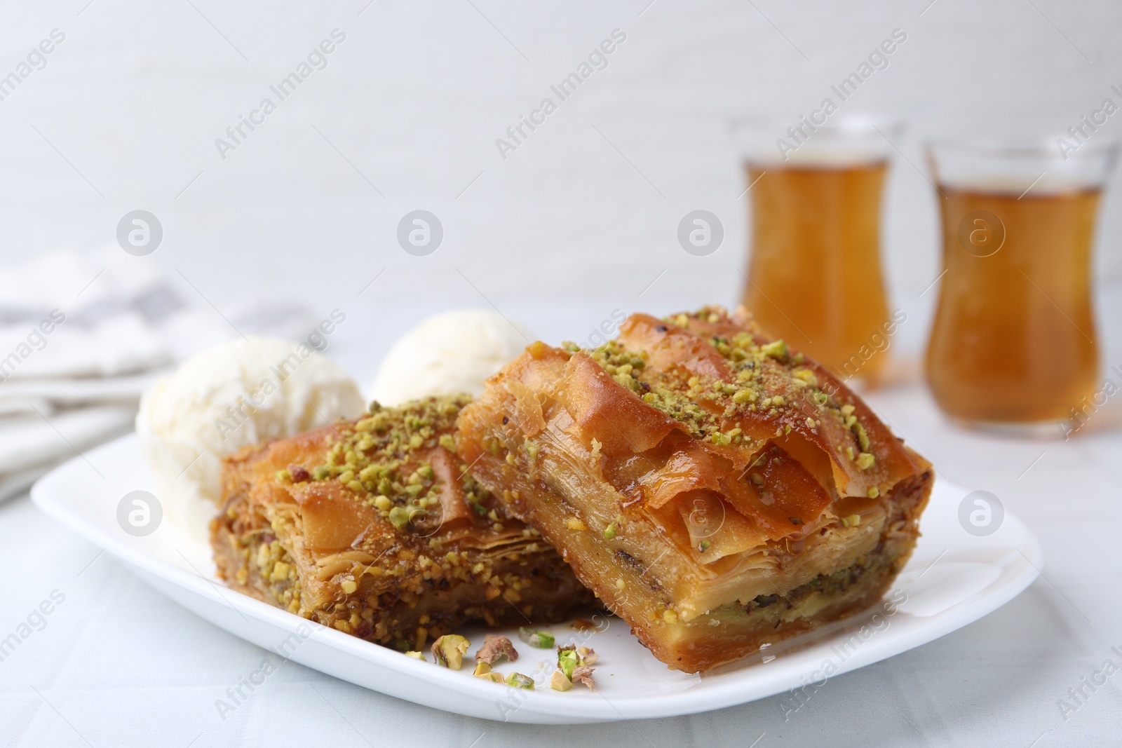 Photo of Delicious baklava with crushed nuts and ice cream on white tiled table, closeup