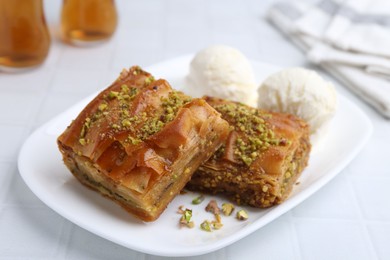 Delicious baklava with crushed nuts and ice cream on white tiled table, closeup