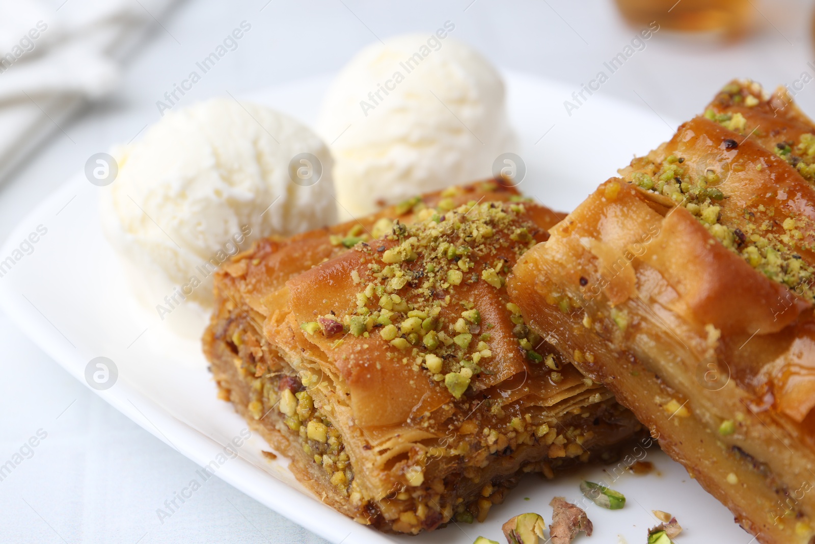 Photo of Delicious baklava with crushed nuts and ice cream on white tiled table, closeup