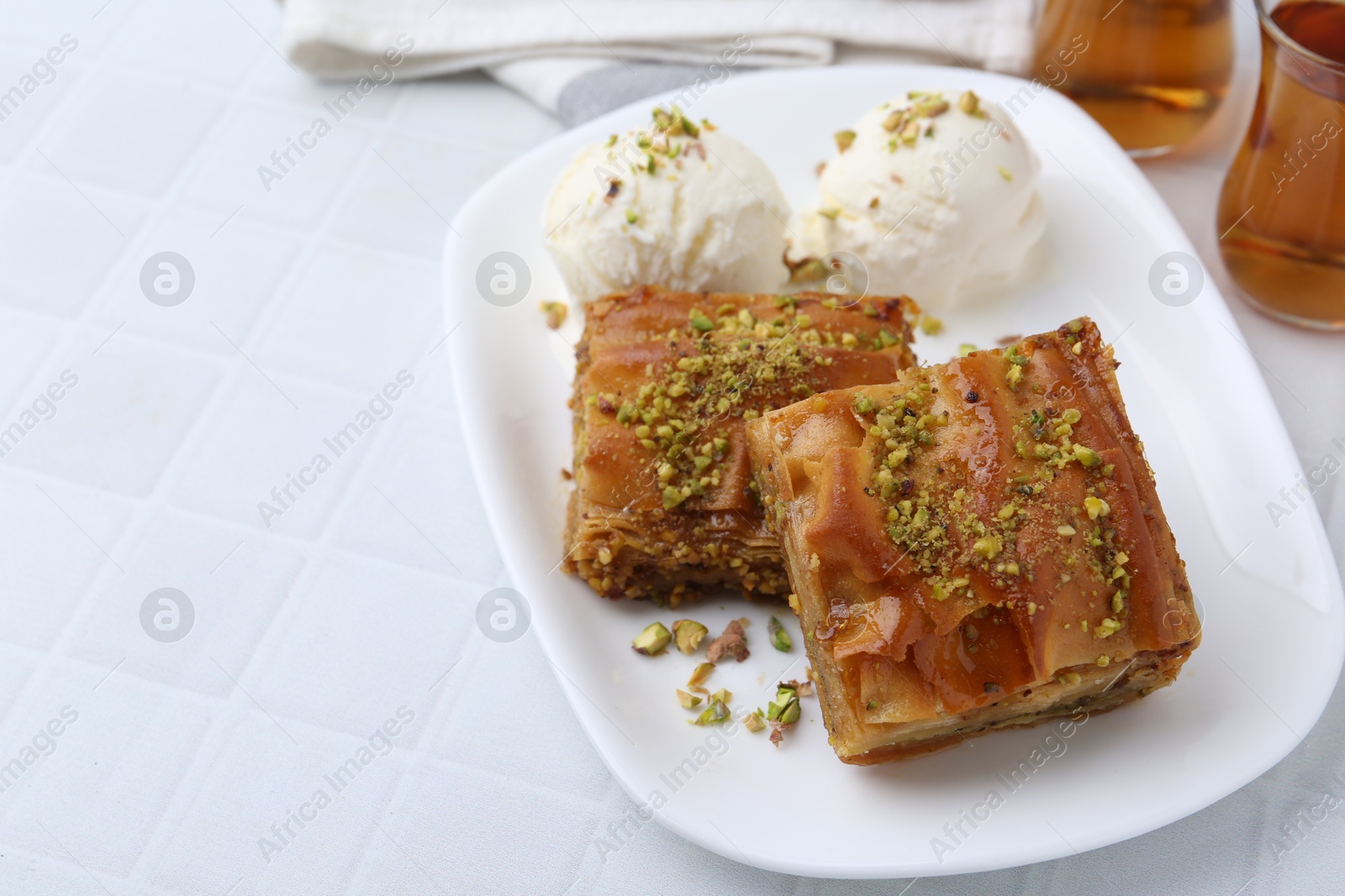 Photo of Delicious baklava with crushed nuts and ice cream on white tiled table, closeup. Space for text