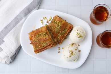 Delicious baklava with crushed nuts and ice cream served on white tiled table, flat lay