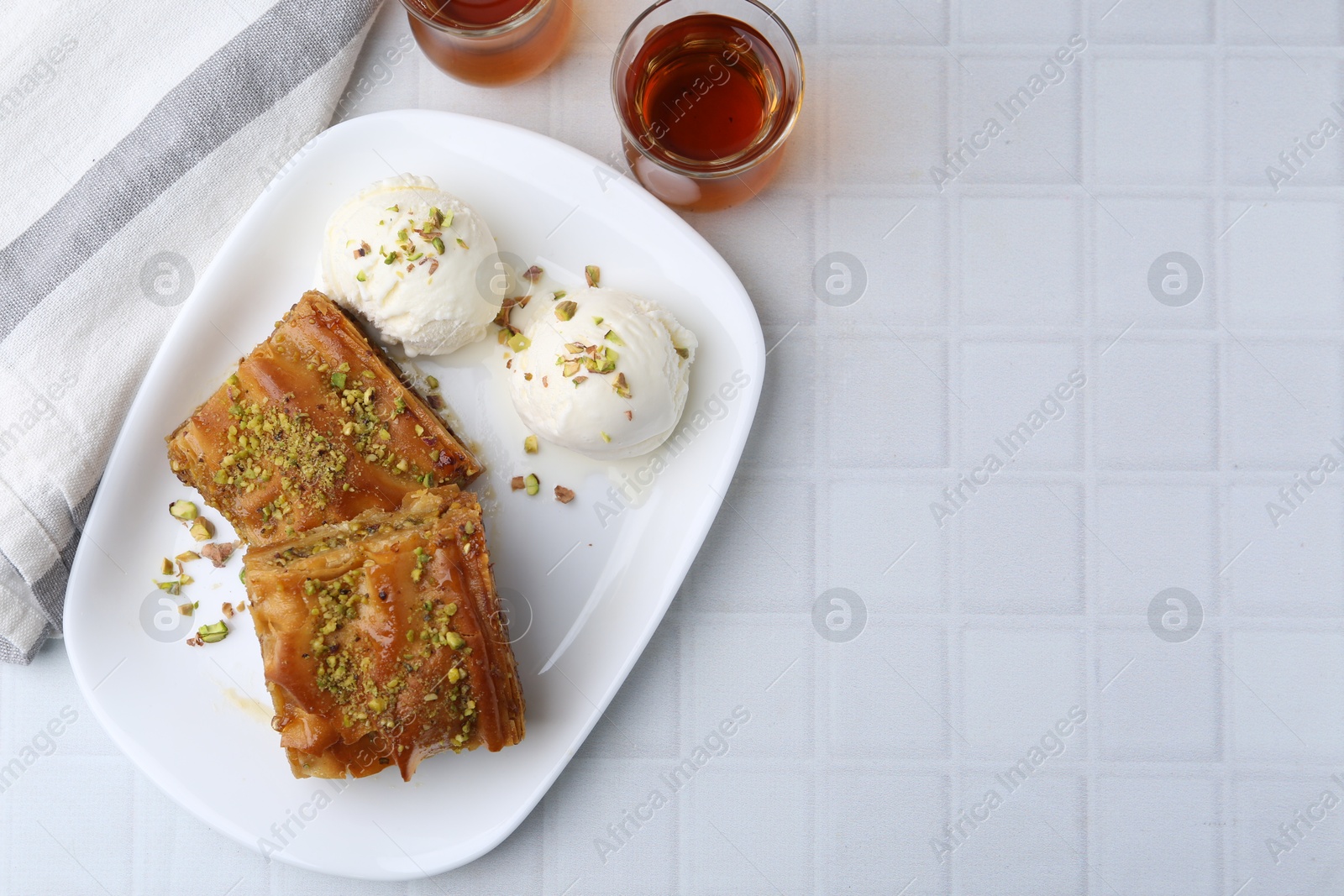 Photo of Delicious baklava with crushed nuts and ice cream served on white tiled table, flat lay. Space for text