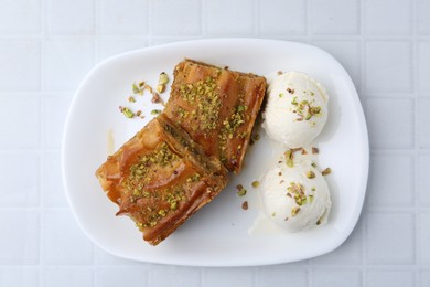 Photo of Delicious baklava with crushed nuts and ice cream on white tiled table, top view