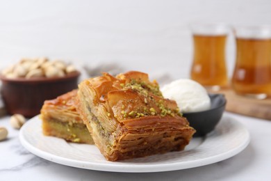 Delicious baklava with crushed nuts and ice cream on white marble table, closeup