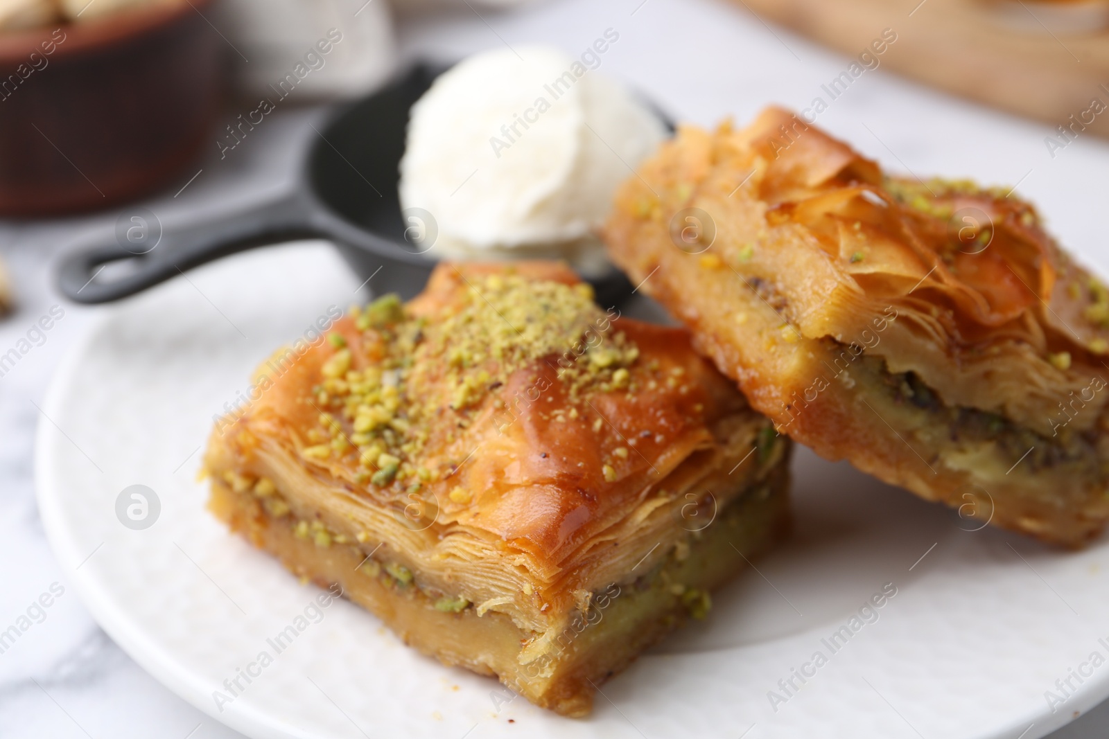 Photo of Delicious baklava with crushed nuts and ice cream on white table, closeup