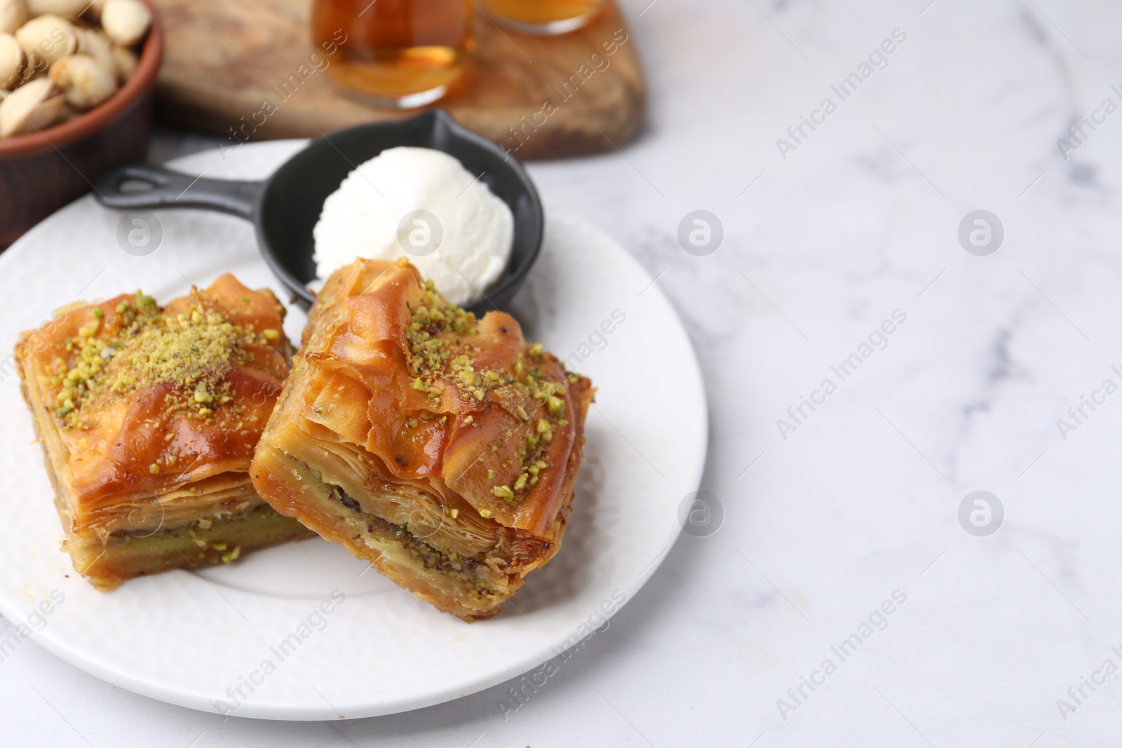 Photo of Delicious baklava with crushed nuts and ice cream on white marble table, closeup. Space for text