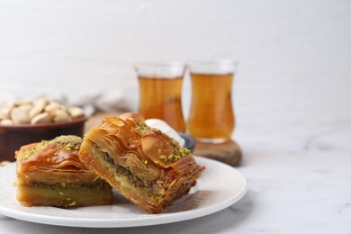 Photo of Delicious baklava with crushed nuts and ice cream on white marble table, closeup. Space for text