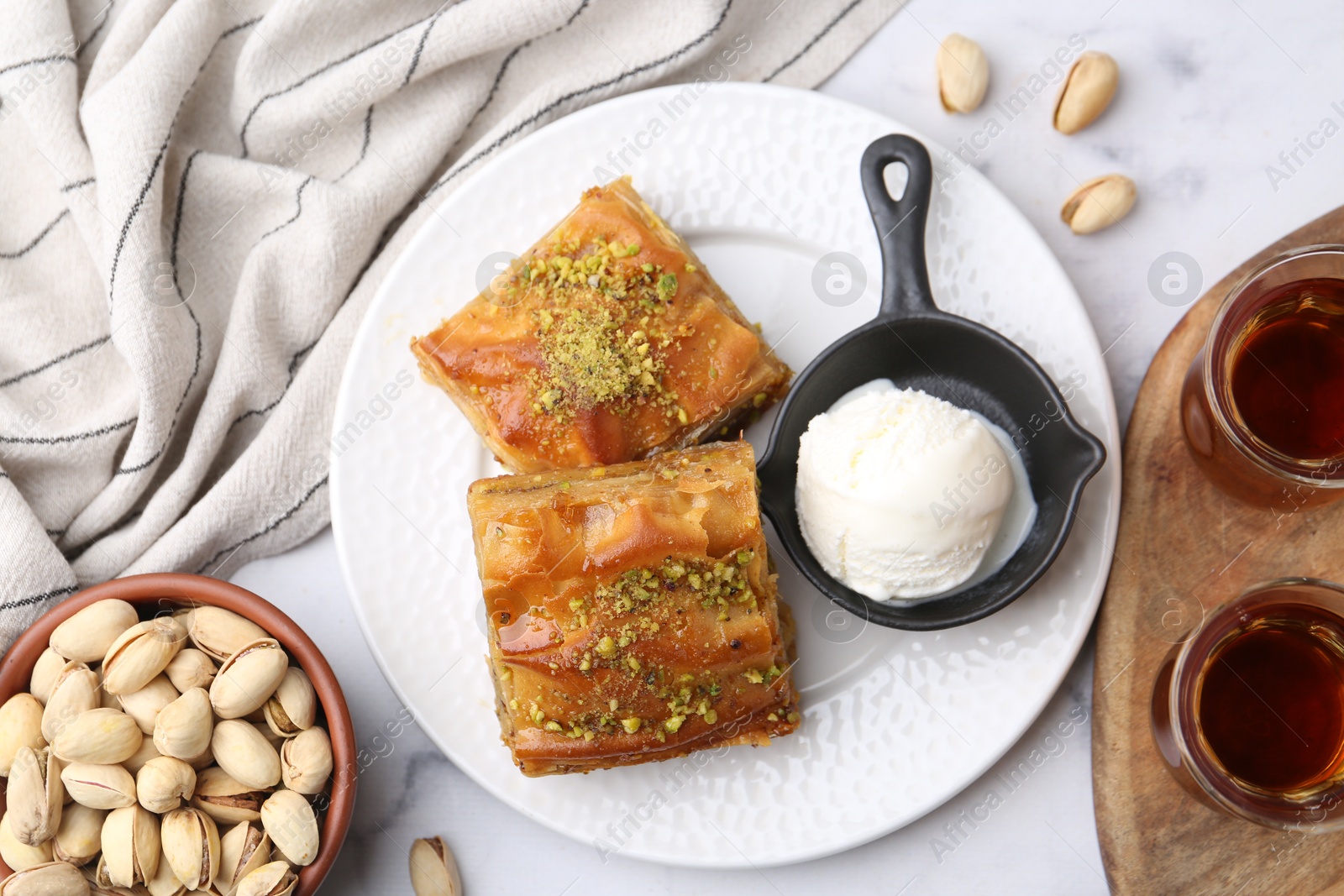 Photo of Delicious baklava with crushed nuts and ice cream served on white marble table, flat lay