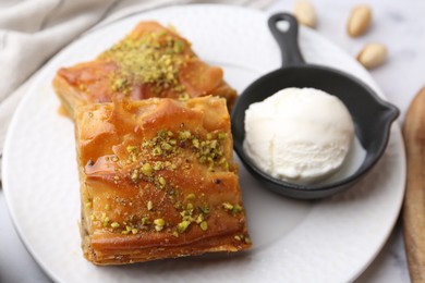 Delicious baklava with crushed nuts and ice cream on table, closeup