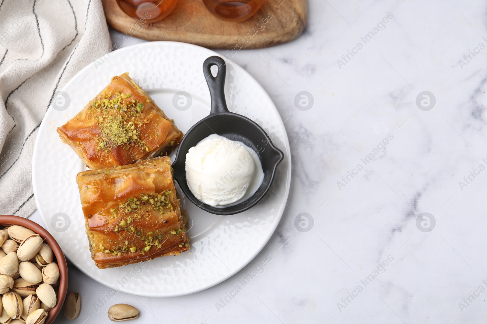 Photo of Delicious baklava with crushed nuts and ice cream on white marble table, flat lay. Space for text