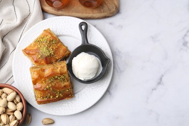 Delicious baklava with crushed nuts and ice cream on white marble table, flat lay. Space for text