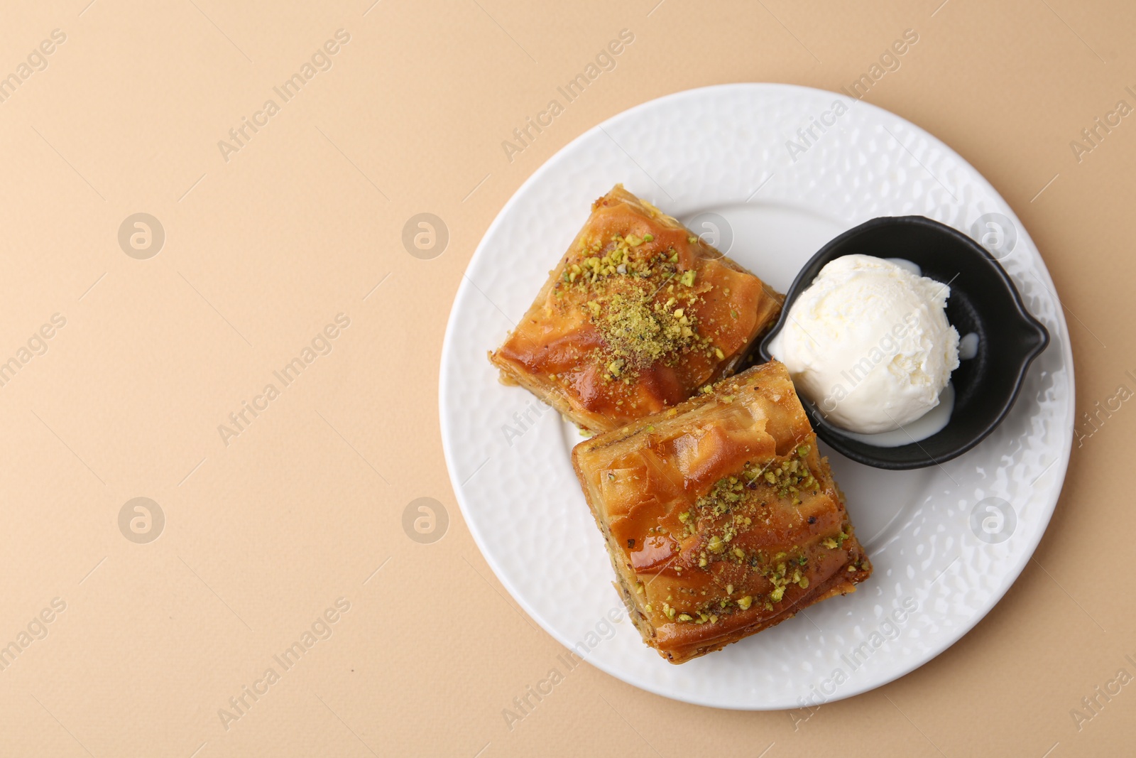 Photo of Delicious baklava with crushed nuts and ice cream on beige table, top view. Space for text