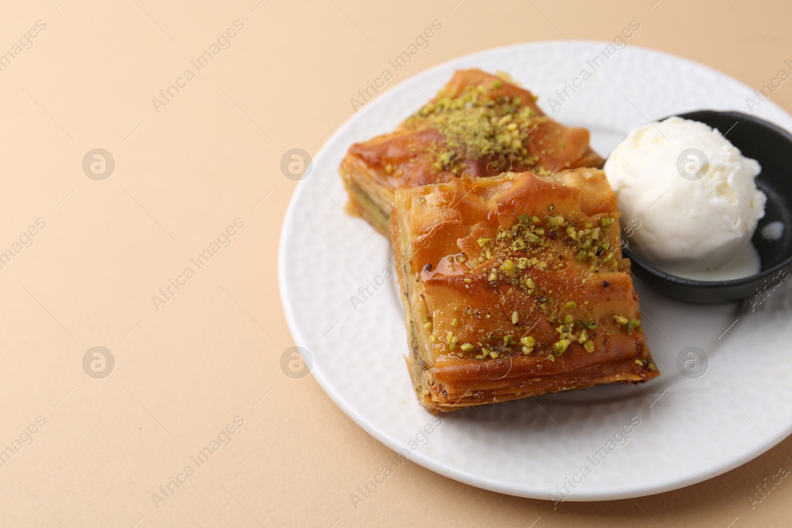 Photo of Delicious baklava with crushed nuts and ice cream on beige table, closeup. Space for text