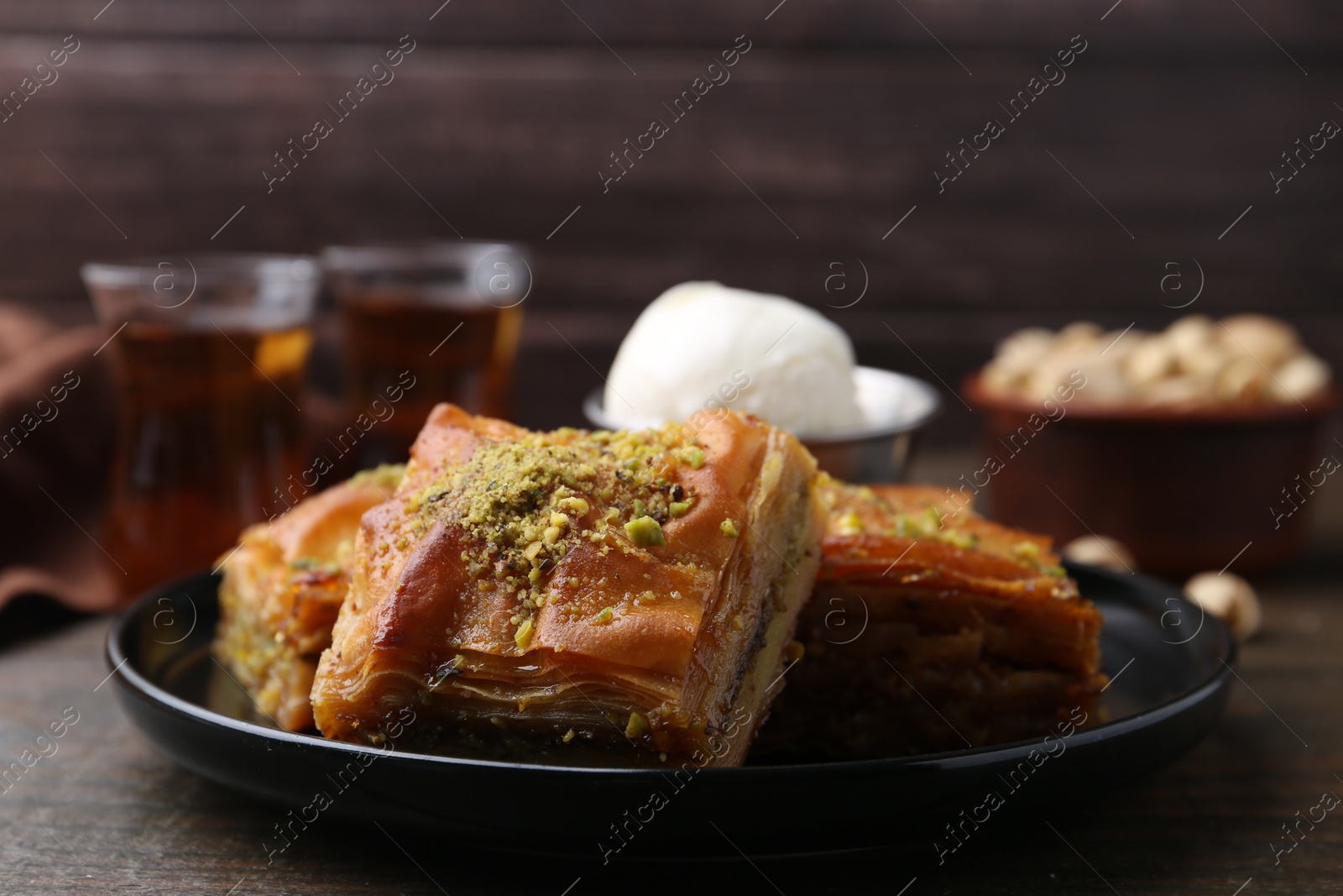 Photo of Delicious baklava with crushed nuts and ice cream on wooden table, closeup