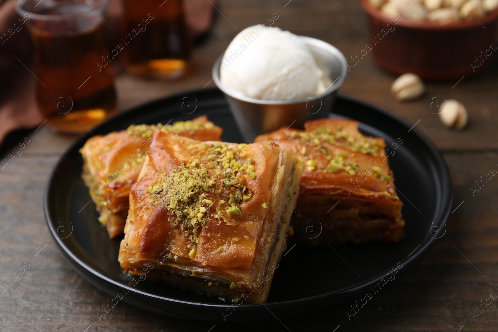 Photo of Delicious baklava with crushed nuts and ice cream on wooden table, closeup