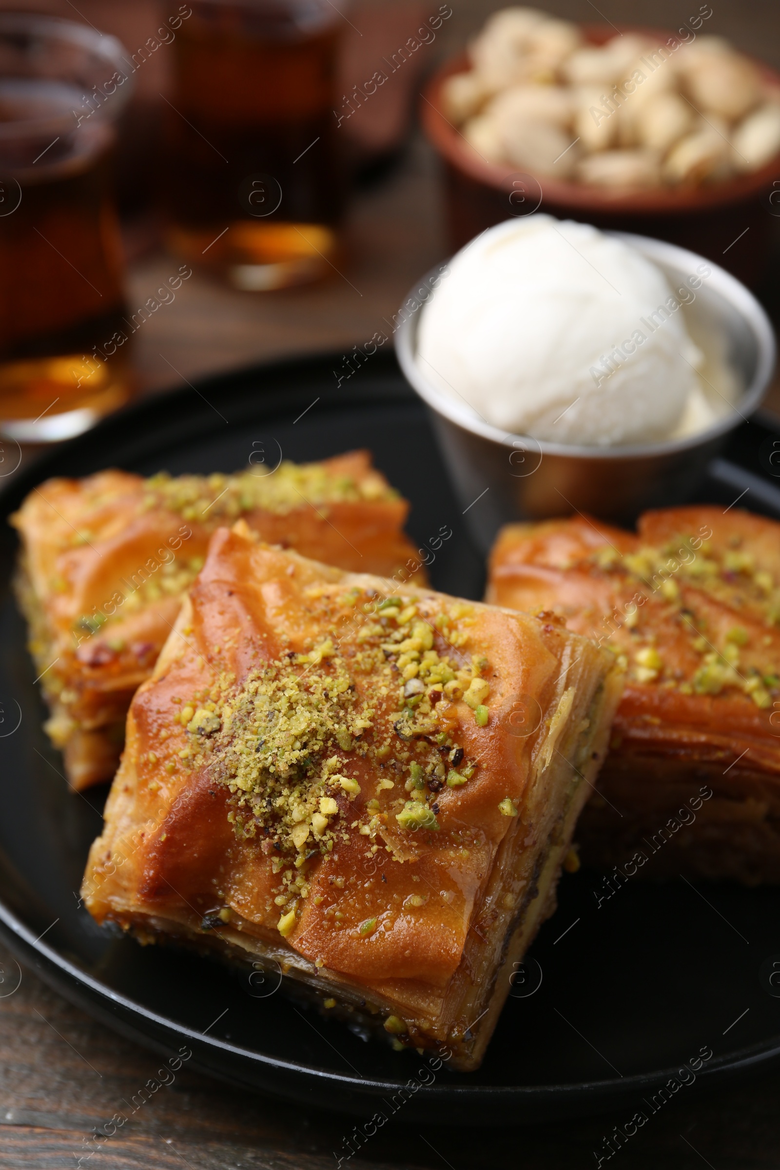 Photo of Delicious baklava with crushed nuts and ice cream on wooden table, closeup