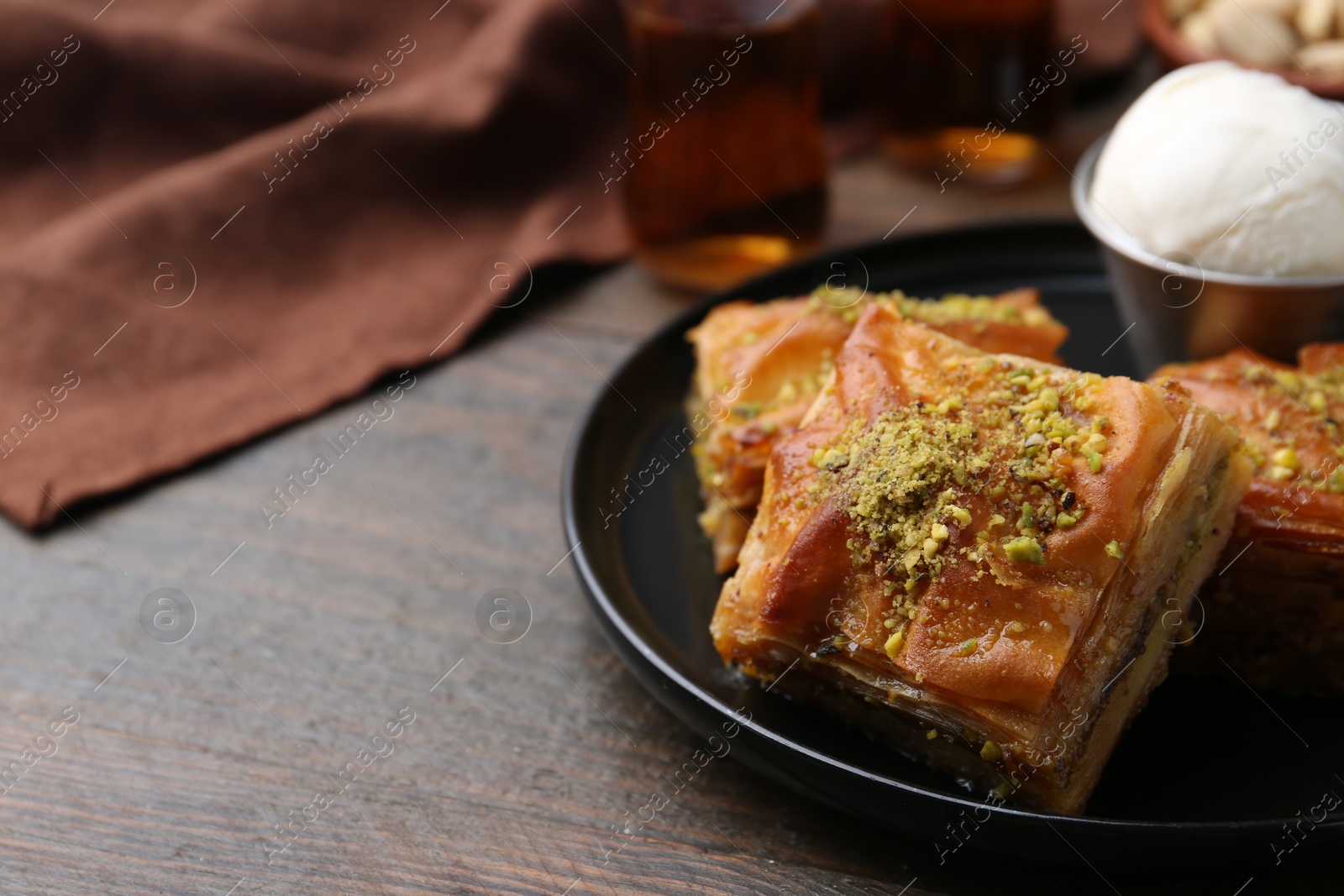 Photo of Delicious baklava with crushed nuts and ice cream on wooden table, closeup. Space for text