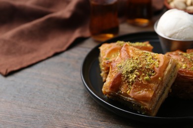 Delicious baklava with crushed nuts and ice cream on wooden table, closeup. Space for text